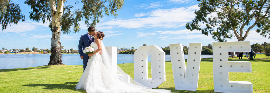 Bride and groom celebrating their wedding at ClubMulwala beside Lake Mulwala, with waterfront views and large LOVE letters at the lakeside wedding venue.